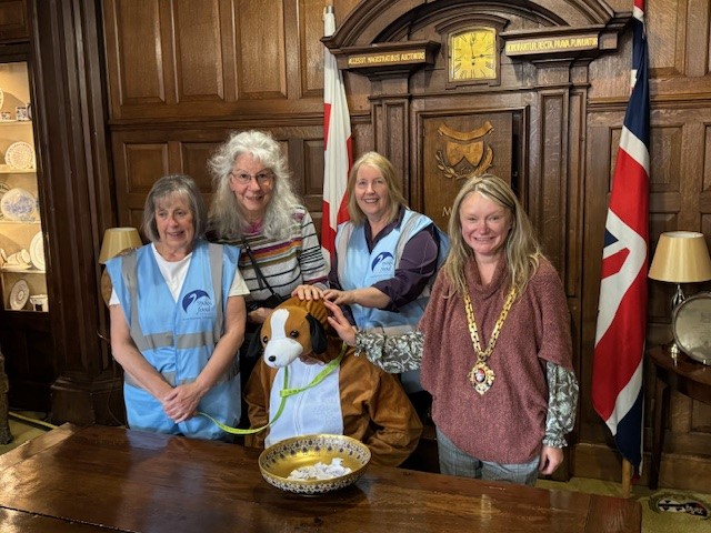 The Mayor with volunteers from the Swan Food project and a dog puppet, standing with a plate full of raffle tickets