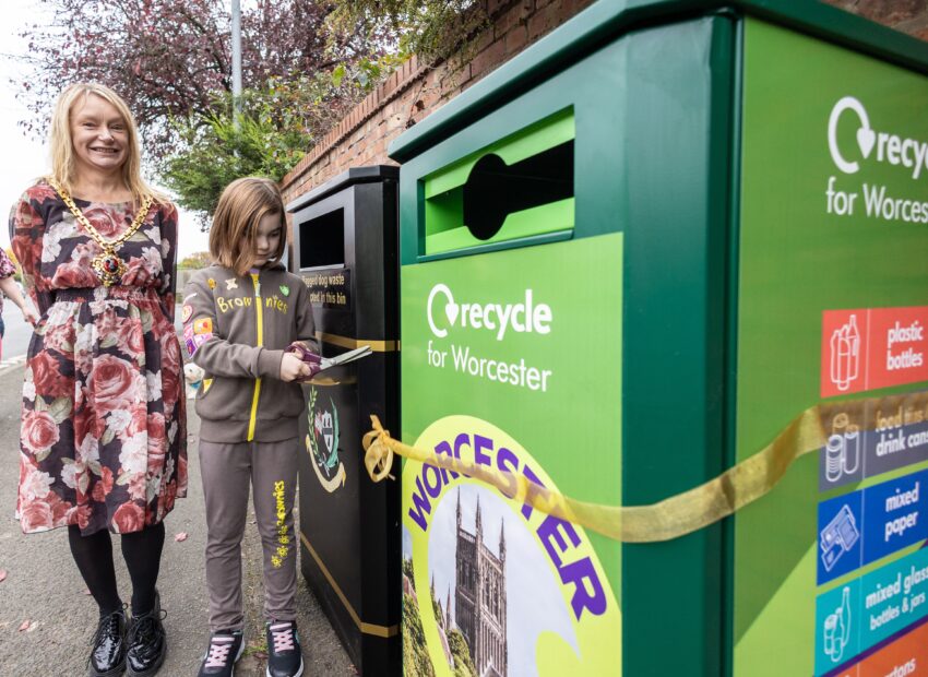 The Mayor and Brownie Lois Burd cutting a ribbon that is tied around a black litter bin and a green recycling bin