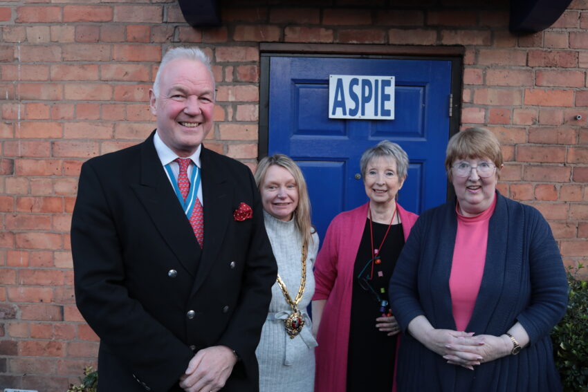 Four people stood by a door with a sign saying ASPIE on